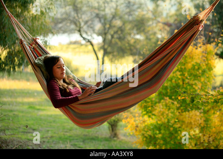 Un giovane adolescente in età ragazza legge in una amaca al tramonto Foto Stock