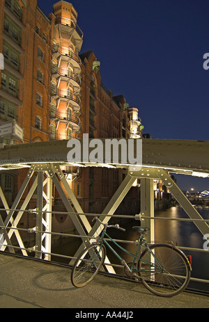 Una bicicletta si appoggia contro un ponte illuminato al vecchio magazzino district Speicherstadt di Amburgo, Germania Foto Stock