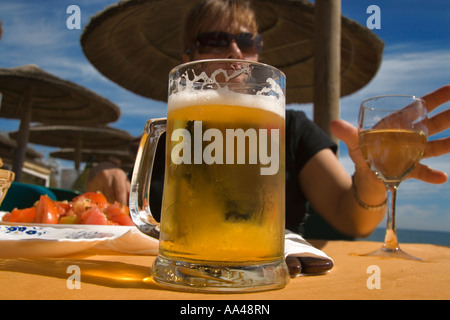 Close up di un fresco bicchiere di birra coperto con condensazione con un'immagine sfocata di una donna Foto Stock
