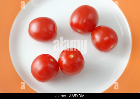 ANG103745 frutta vegetali rossi pomodori bambino sulla piastra bianca su sfondo arancione Foto Stock