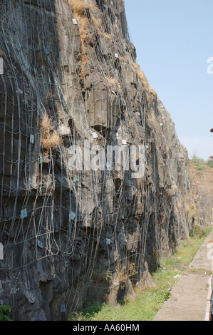 Rete di filo di acciaio inchiodato in rocce tenere allentata della frana di rocce del taglio ripida collina di passare Konkan Railway Foto Stock