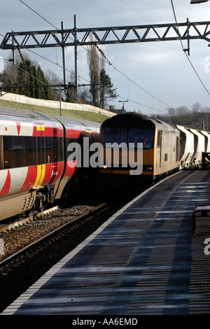 Treno merci passando attraverso Crossflatts stazione treno passeggeri fermo sulla linea opposta Foto Stock