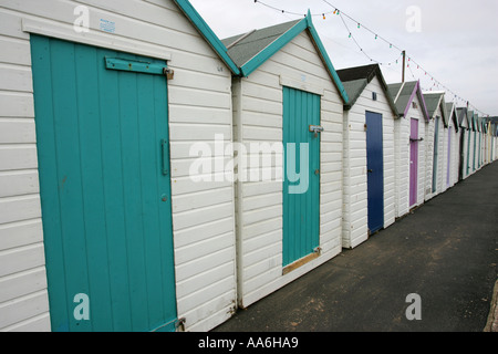 Lungo la linea di riga di bianca spiaggia Vittoriano di capanne con dipinto luminosamente sportelli sul lungomare di Paignton Devon England Gran Bretagna Foto Stock