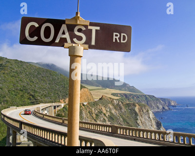 COAST ROAD SEGNO CALIFORNIA BIXBY BRIDGE BIG SUR DRIVE VACANZA SUN Coast Road segno, auto rossa che attraversa Bixby Bridge a Big sur, Monterey, California Stati Uniti Foto Stock