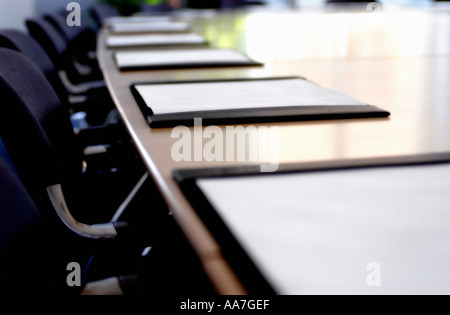Sedie nere e blotter pad in pelle su un lungo tavolo in legno in una sala riunioni vuota Foto Stock