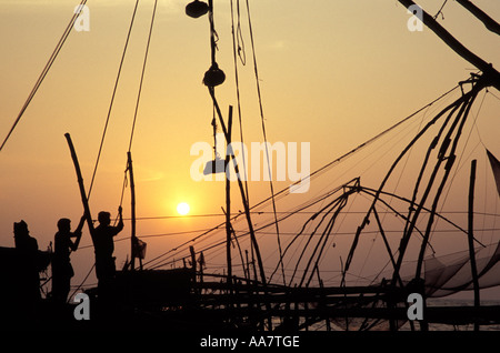 Pescatori indiani che trasportano reti da pesca cinesi al tramonto, Kochi, India meridionale Foto Stock