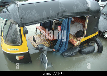 Inondazioni dovute a piogge monsoniche mostra driver dormire in auto rickshaw in acqua allagata Mumbai India Foto Stock