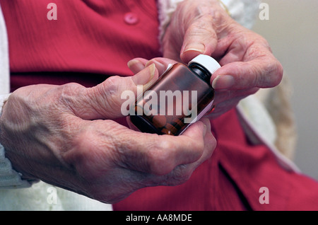 Una signora anziana con artrite severa cercando di aprire una bottiglia di pillole Foto Stock