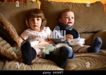 Due bambini di mangiare uno spuntino e guardare la televisione. Foto Stock