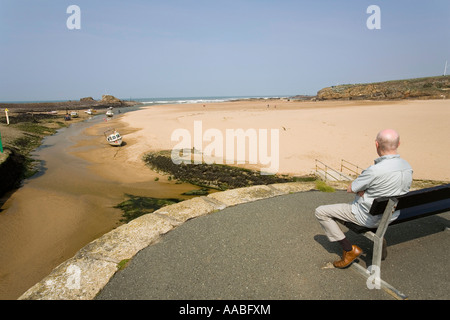 Regno Unito Cornovaglia Bude Haven uomo su una panchina affacciata Summerleaze Beach Foto Stock