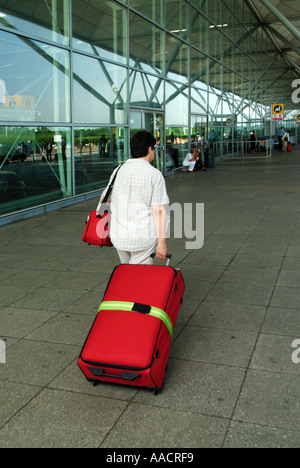 Modello di vista posteriore rilasciato donna passeggero delle festività che tira una valigia rossa per salire a bordo di un volo dall'aeroporto Stansted di Londra Essex Inghilterra Regno Unito Foto Stock