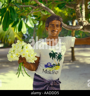 Giovani Maldivan sorridente uomo in bianco t-shirt holding mazzetto di fiori di frangipani su un isola Bandos alle Maldive Foto Stock