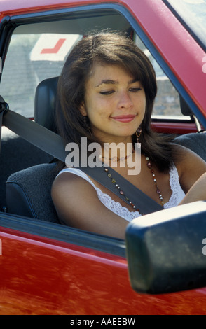 Felice attraente ragazza adolescente donna giovane allievo conducente cercando nel suo specchietto retrovisore Foto Stock
