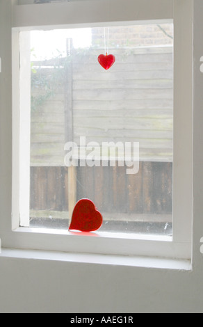 Vetro rosso cuori appeso sul filo accanto a una finestra della cucina, Londra, Regno Unito, maggio 2007. Foto Stock