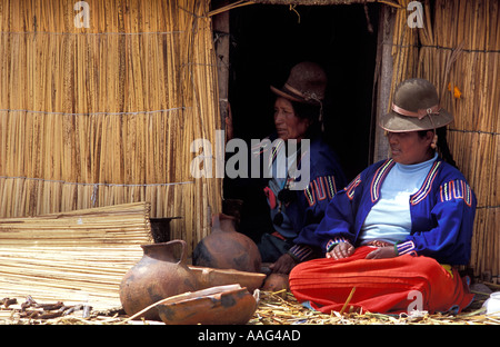 Due Uros isolani in seduta e accanto a casa loro fatta da ance pentole a secco di pesce di fronte al lago Titicaca vicino a Puno Foto Stock