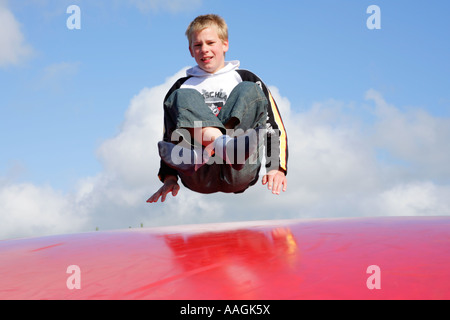 Un giovane ragazzo che rimbalza su un grande trampolino di gomma Foto Stock