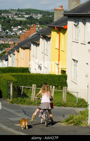 Ragazza giovane ciclismo tenendo cane per camminare su una autorità locale consiglio case station wagon Penparcau Aberystwyth Ceredigion REGNO UNITO GALLES Foto Stock