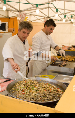 Due maschi cuochi francesi preparare grandi pan di fresco il cibo caldo su un mercato in stallo Aberystwyth Ceredigion nel Galles Foto Stock