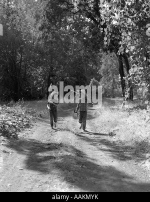 Negli anni quaranta anni cinquanta due ragazzi in salopette da PLAID camicie di cappelli di paglia camminare per strada sterrata porta pali pesca & possibile di esche Foto Stock