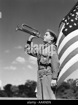 Anni Cinquanta PROFILO DI BOY SCOUT IN UNIFORME IN PIEDI DI FRONTE A 48 stelle della bandiera americana BUGLE di soffiatura Foto Stock