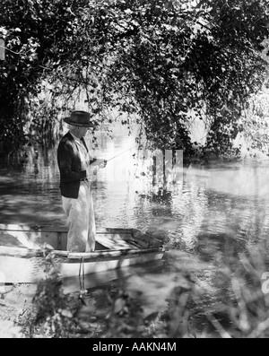 1940s uomo anziano IN HAT IN PIEDI IN canotto pesca sotto gli alberi Foto Stock