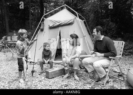 Anni Settanta la famiglia di quattro seduti nella parte anteriore della tenda in boschi figlio azienda pesca polo in una mano e il grande pesce IN ALTRI Foto Stock