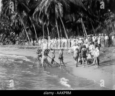 1920s film equipaggio con telecamere su treppiedi in surf sulla spiaggia tropicale Foto Stock