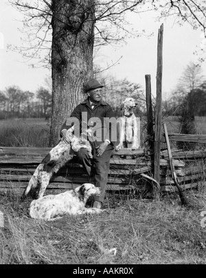 1920s uomo & tre cani seduti sul recinto il suo fucile è appoggiata sul recinto accanto a lui Foto Stock