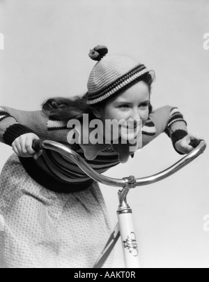 1930s desiderosa sorridente bambina in berretto IN MAGLIA E MATCHING MAGLIONE equitazione Bicicletta appoggiata nel manubrio Foto Stock