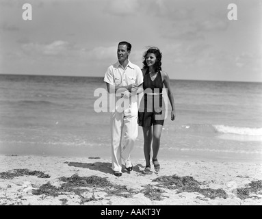 1930s giovane sotto braccio fino a piedi da Ocean uomo sorridente in camicia bianca e pantaloni DONNA IN DARK HALTER TOP & SHORTS Foto Stock