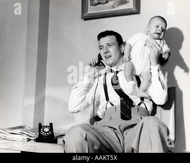 Degli anni Cinquanta padre tenendo il bambino mentre si è al telefono Foto Stock