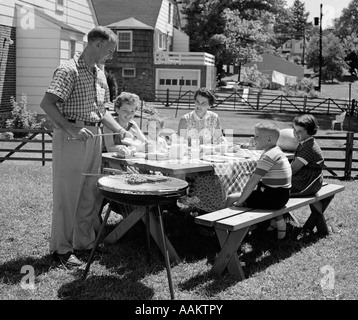 Degli anni Cinquanta la FAMIGLIA IN CORTILE LA COTTURA DI HOT DOG seduti al tavolo da picnic Foto Stock