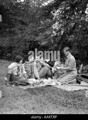 1920s QUATTRO PERSONE DUE COPPIE UOMINI DONNE seduta sul terreno godendo un picnic Foto Stock