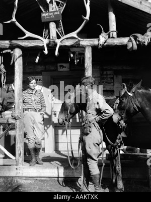 1920s 1930 GIOVANE E CAVALLI NELLA PARTE ANTERIORE DEL WESTERN Hunting Lodge portico con trofeo palchi teschi BRAZEAU lago Alberta Foto Stock