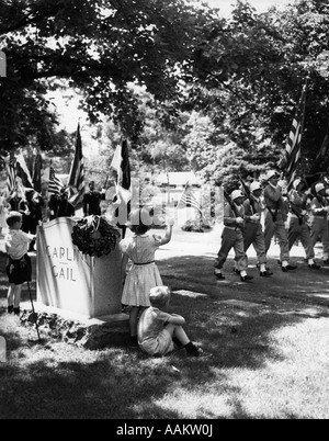 Anni Cinquanta un ragazzo e una ragazza di stand da parte di un oggetto contrassegnato per la rimozione definitiva AGITANDO PER PASSARE COLOR GUARD DI SOLDATI IN UN GIORNO MEMORIALE DELLA SFILATA Foto Stock