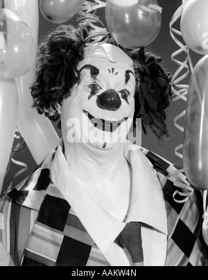 Anni sessanta ritratto WHITEFACE CLOWN IN COSTUME completo circondato da palloncini guardando la fotocamera Foto Stock