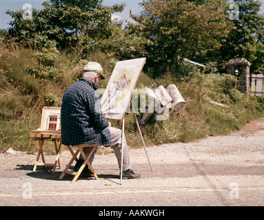 Anni sessanta anziani SENIOR ALL'APERTO uomo seduto alla pittura di cavalletto una fila di caselle di posta Foto Stock