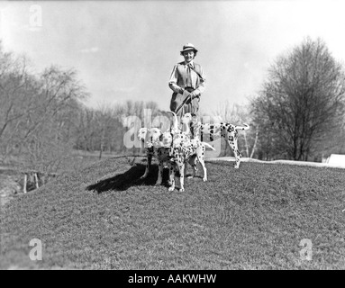 1930s donna sorridente a piedi legato quattro cani dalmata Foto Stock