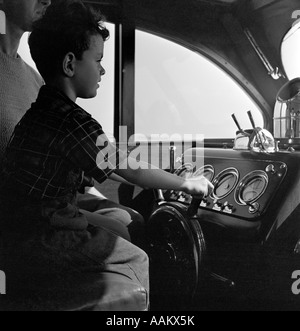 1940s ragazzo seduto al volante delle navi di motor yacht con padre dietro Foto Stock