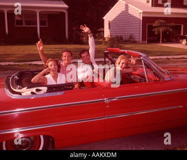 Anni sessanta due coppie giovani in rosso convertibili automobile sulla strada suburbana ridere agitando mani guardando la fotocamera Foto Stock
