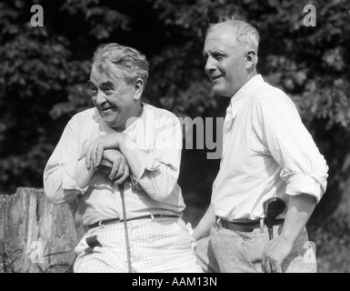 1920s 1930 2 uomini anziani holding club di golf seduti su un ceppo di albero GUARDANDO VERSO IL CAMPO DA GOLF Foto Stock