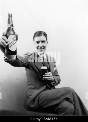 1930s uomo tenendo premuto fino enorme distorta BOTTIGLIA DI BIRRA IN UNA MANO E UNA DIMENSIONE REGOLARE UN BICCHIERE DI BIRRA IN ALTRI sorridente guardando la fotocamera Foto Stock