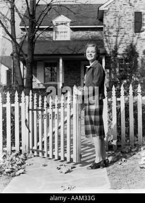 1940s sorridente piuttosto giovane ragazza adolescente IN PIEDI DA WHITE Picket Fence davanti casa di pietra IN AUTUNNO Foto Stock