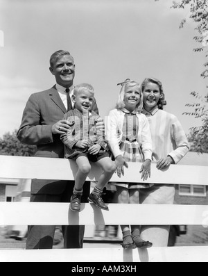 Anni Cinquanta ritratto di famiglia padre uomo donna madre figlia ragazza ragazzo figlio dietro il recinto del cortile sorridente verso la telecamera Foto Stock