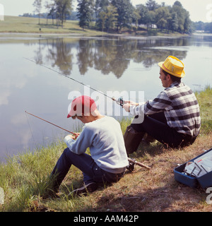 Negli anni settanta il ragazzo uomo seduto in riva al fiume lago pesca sportiva padre figlio famiglia FAMIGLIE Foto Stock