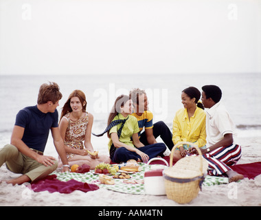 Anni Settanta ETNIA coppie adolescenti picnic sulla spiaggia Foto Stock