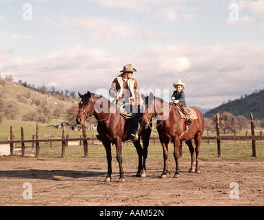 Anni Settanta uomo COWBOY padre e figlio del ragazzo seduto insieme su cavalli da CORRAL indossando cappelli IN CALIFORNIA USA Foto Stock