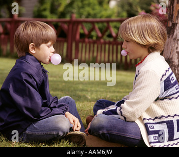 Anni Settanta Bambini ragazza ragazzo sedersi FACCIA A FACCIA INDOSSARE MAGLIONI JEANS BLU SOFFIARE SOFFIAGGIO BOLLE ROSA CON BOLLA DI CHEWING GUM Foto Stock