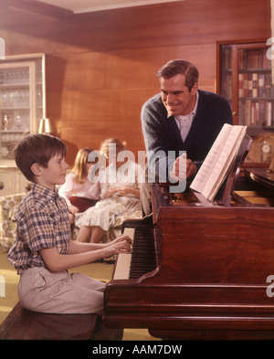 1970 anni settanta SALOTTO BOY figlio suonando piano padre ascolto ragazza madre figlia del lettino famiglie di sfondo Foto Stock