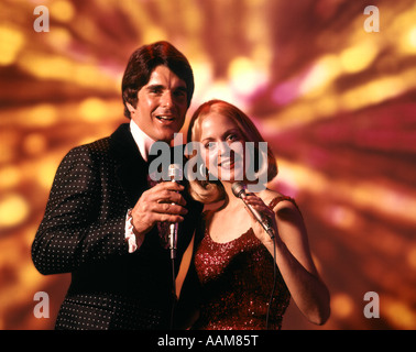 1970 anni settanta uomo donna cantanti cantare cantante DONNA BIONDA vestito rosso tenere il microfono uomo TUXEDO animatori Foto Stock